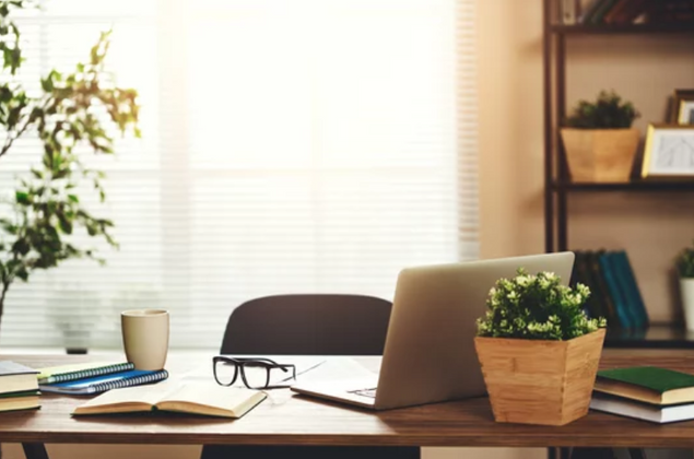 an open laptop sits on a wooden desk in front of a window of a CEO or Assistant